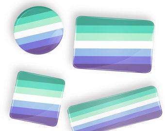 Puede incluir: Cuatro botones de diferentes tamaños con los colores de la bandera del orgullo genderqueer. La bandera tiene cinco franjas: verde claro, blanco, azul claro, azul oscuro y morado.