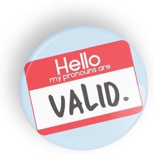 May include: A red and white name tag with the text "Hello my pronouns are VALID." on a light blue background.