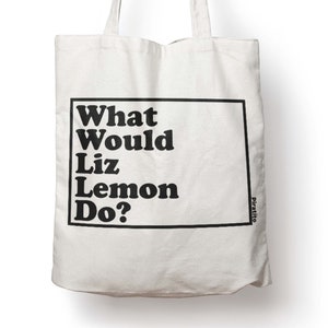 Puede incluir: Bolsa de tela blanca de lona con texto negro que dice "What Would Liz Lemon Do?" en negrita. El texto está encerrado en un rectángulo negro. La palabra "piratito" está impresa en negro en la esquina inferior derecha de la bolsa.