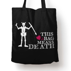 May include: Black tote bag featuring a white skeleton graphic holding a sword and a heart. The text "THIS BAG MEANS DEATH" is printed in white. The bag has two black handles.