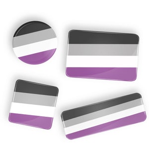 Puede incluir: Cuatro botones de diferentes tamaños con la bandera del orgullo asexual. La bandera es negra, gris, blanca y morada.