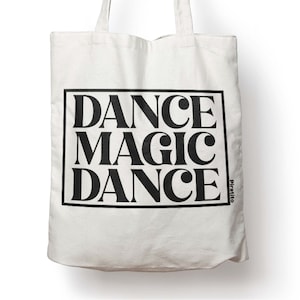 Può includere: Borsa tote in tela bianca con testo nero che recita "DANCE MAGIC DANCE" in un carattere audace retrò. Il testo è racchiuso in un rettangolo nero. La parola "piratito" è stampata in piccole lettere nere nell'angolo in basso a destra della borsa.