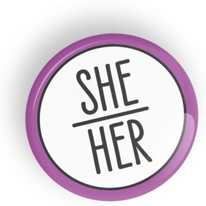 以下が含まれることがあります： 黒文字で「SHE / HER」と書かれた、紫と白のボタンです。