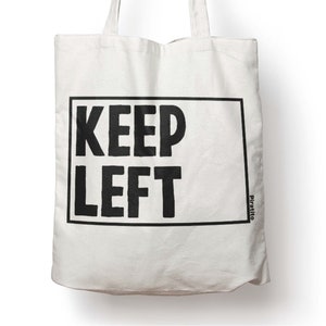 Può includere: Borsa tote in tela bianca con testo nero che recita "KEEP LEFT" in un riquadro. Il testo "Piratito" è stampato nell'angolo in basso a destra.