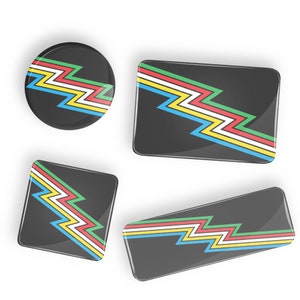 May include: Four black buttons with a colorful zigzag pattern. The buttons are in different sizes and shapes.