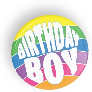 May include: A round button with a rainbow stripe design. The text "Birthday Boy" is written in white on the button.