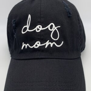 May include: A black distressed baseball cap with white embroidered text that reads "dog mom".