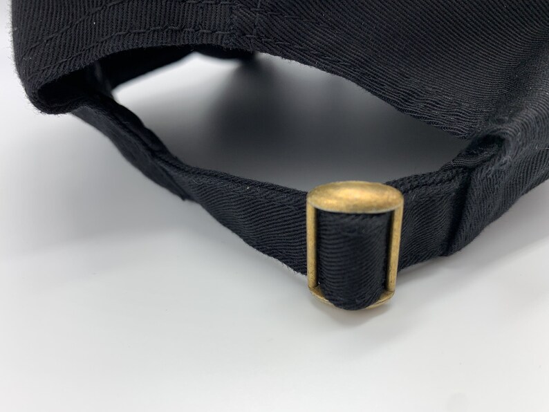 May include: Close-up of the back of a black baseball cap with a gold metal adjustable strap.