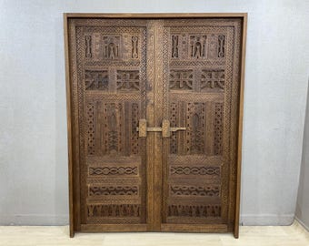 May include: A pair of intricately carved wooden doors. The doors are a warm brown color and feature detailed geometric and stylized designs. A wooden latch secures the doors. The doors are framed in a matching wood.
