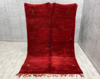 May include: A red Moroccan rug with a geometric pattern. The rug has a fringe border and is made of wool.