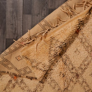 Pu&ograve; includere: Un tappeto tessuto beige e marrone con un bordo a frangia. Il tappeto &egrave; piegato a met&agrave;, mostrando la trama della tessitura.