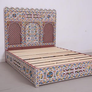 May include: A decorative bed frame with a headboard and footboard. The frame is painted with intricate geometric patterns in shades of red, blue, yellow, and white. The bed frame has a wooden slat base.