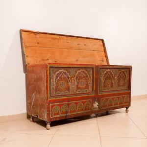May include: A wooden chest with a hinged lid, painted in red, gold and blue with intricate geometric patterns. The chest is decorated with traditional Moroccan designs.