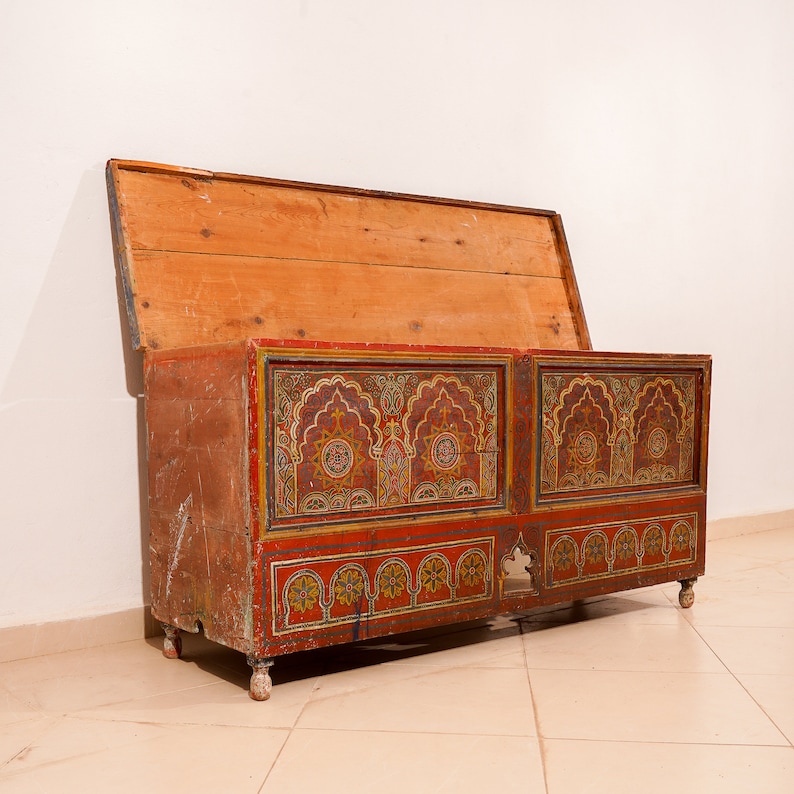 May include: A wooden chest with a hinged lid, painted in red, gold and blue with intricate geometric patterns. The chest is decorated with traditional Moroccan designs.