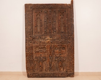 May include: A dark brown wooden door with intricate carvings and metal accents. The door is made of thick wood and has a rustic appearance.