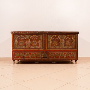 May include: A large, intricately carved wooden chest with a red, gold, and black paint scheme. The chest has a decorative design of arches and geometric patterns.