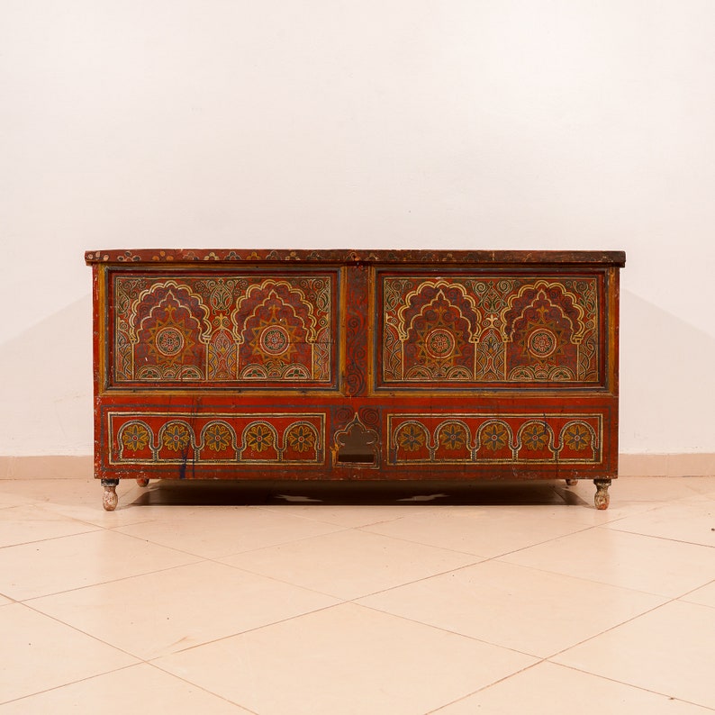 May include: A large, intricately carved wooden chest with a red, gold, and black paint scheme. The chest has a decorative design of arches and geometric patterns.