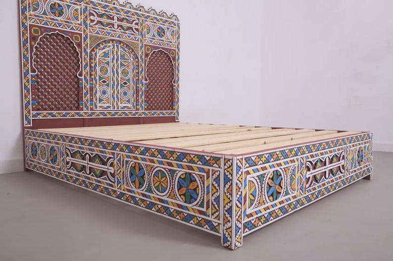 May include: A decorative bed frame with a headboard and footboard. The frame is painted with intricate geometric patterns in white, blue, yellow, and red. The headboard features arched designs and a textured brown panel.
