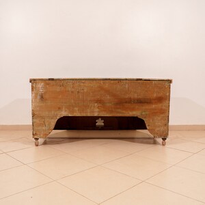 May include: A vintage wooden chest with a light brown finish. The chest has a simple design with a rectangular shape and a slightly curved top. It has a small cutout on the front and rests on four small legs.
