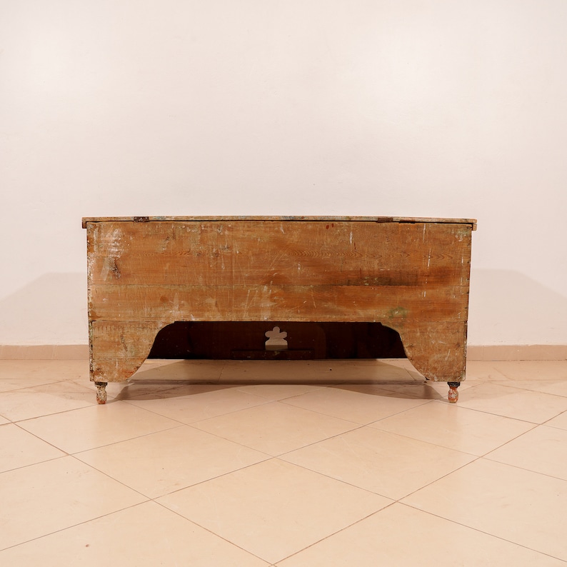 May include: A vintage wooden chest with a light brown finish. The chest has a simple design with a rectangular shape and a slightly curved top. It has a small cutout on the front and rests on four small legs.