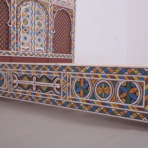 May include: A handcrafted wooden bed frame and headboard with intricate, colourful geometric patterns. The headboard features a decorative arched design. The bed frame is painted with blue, yellow, and orange accents.
