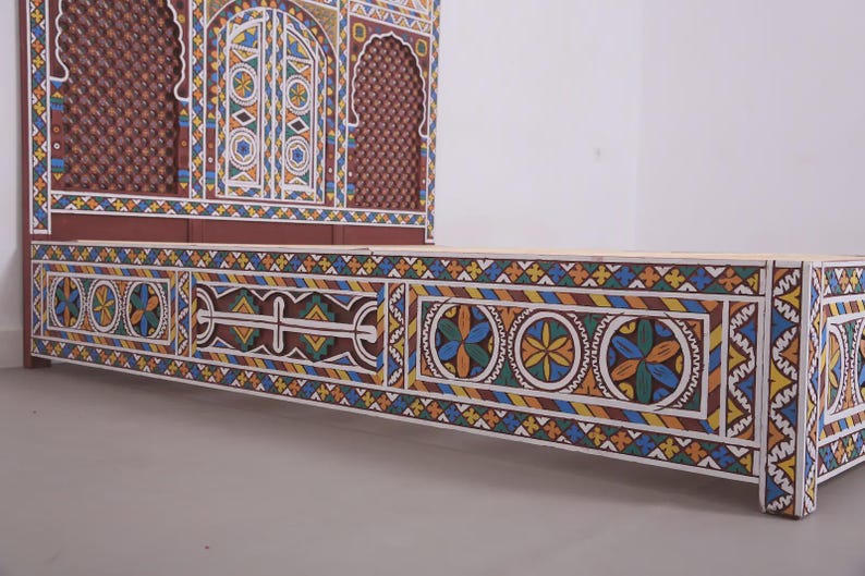 May include: A handcrafted wooden bed frame and headboard with intricate, colourful geometric patterns. The headboard features a decorative arched design. The bed frame is painted with blue, yellow, and orange accents.