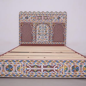 May include: A handcrafted bed frame with intricate, colourful geometric patterns. The headboard features a central arched design with a door motif, flanked by arched panels. The frame is painted in shades of red, blue, yellow, and white, creating a vibrant, decorative piece.