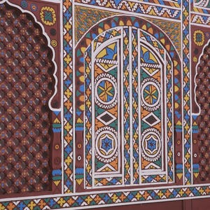 May include: A section of a wall with intricate, colourful geometric designs. The wall features a central arched doorway with detailed patterns in white, blue, yellow, and green. Flanking the doorway are arched panels with a repeating diamond pattern in a reddish-brown hue.