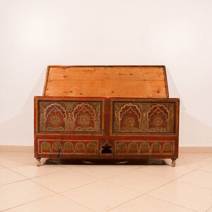May include: A vintage wooden storage chest with intricate painted designs in red, gold, and green. The chest has a hinged lid and is decorated with geometric patterns.