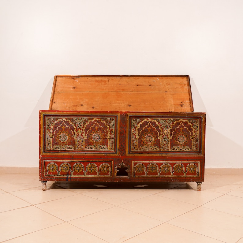 May include: A vintage wooden storage chest with intricate painted designs in red, gold, and green. The chest has a hinged lid and is decorated with geometric patterns.