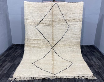May include: A white Moroccan rug with a black diamond pattern. The rug has a fringe border.