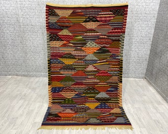 May include: A colorful, geometric patterned rug with a diamond design. The rug is made of wool and has a fringe border.