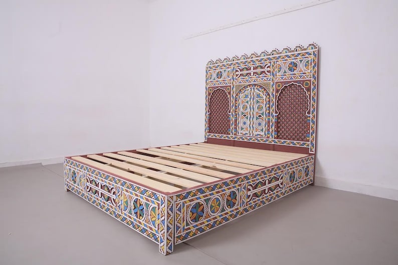 May include: A colourful bed frame with a headboard and footboard. The frame is painted with a geometric pattern in blue, yellow, red, and white. The headboard features an arched design with a patterned background.