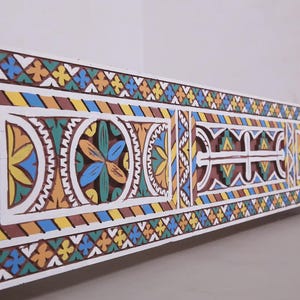 May include: A low-angle view of a white wooden bed frame featuring detailed, colourful geometric patterns. The design incorporates yellow, blue, orange, and brown hues, creating a vibrant aesthetic. The bed frame is a decorative piece.