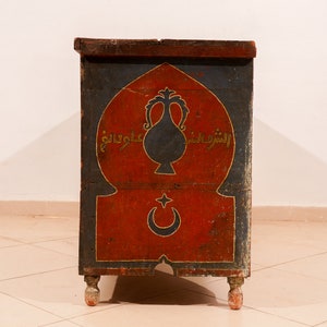 May include: A vintage wooden chest with a red, blue and gold painted design. The chest features an arched top with a crescent moon and star, and Arabic script.