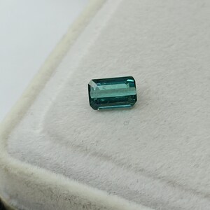 Op de afbeelding: Een teal groene edelsteen met een rechthoekige smaragd-slijpvorm.