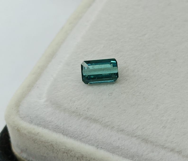 Op de afbeelding: Een teal groene edelsteen met een rechthoekige smaragd-slijpvorm.