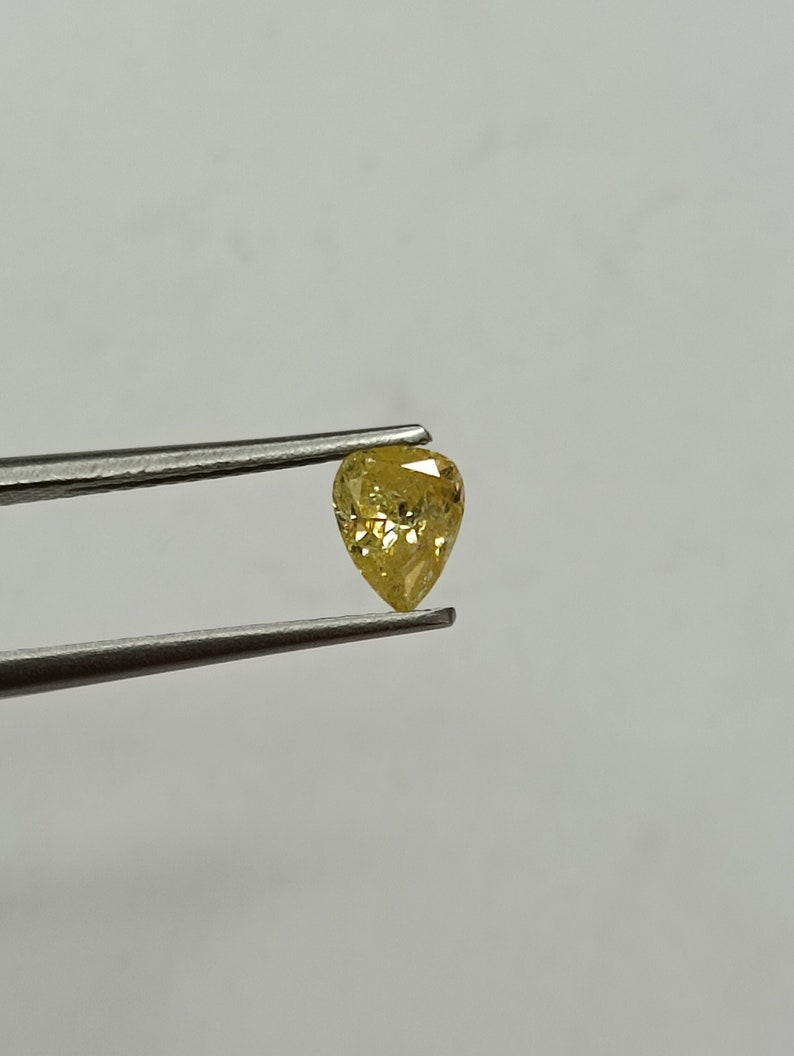 May include: A yellow pear-shaped diamond held by tweezers against a white background.