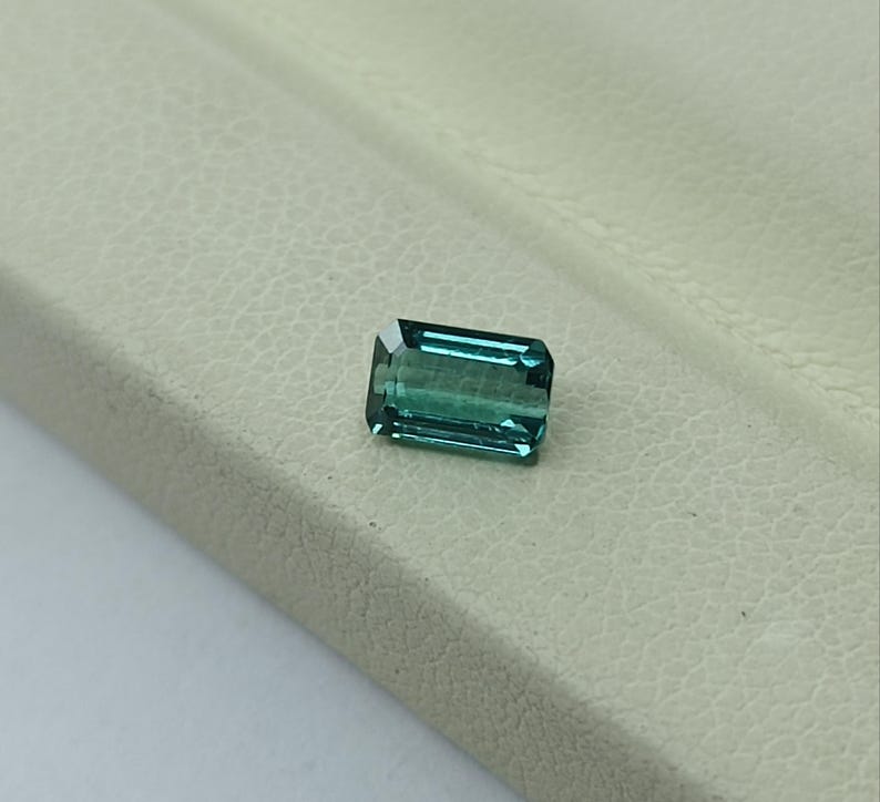 Op de afbeelding: Een teal groene edelsteen met een rechthoekige smaragdslijp.