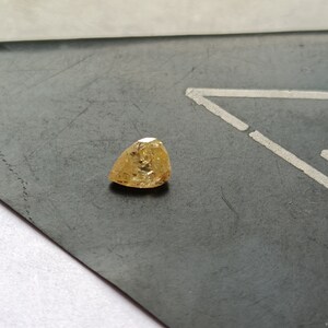 May include: A triangular shaped, yellow gemstone with facets.