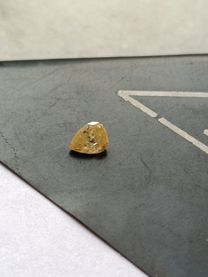 May include: A triangular shaped, yellow gemstone with facets.