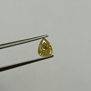 May include: A pear-shaped yellow diamond gemstone held by tweezers against a white background.