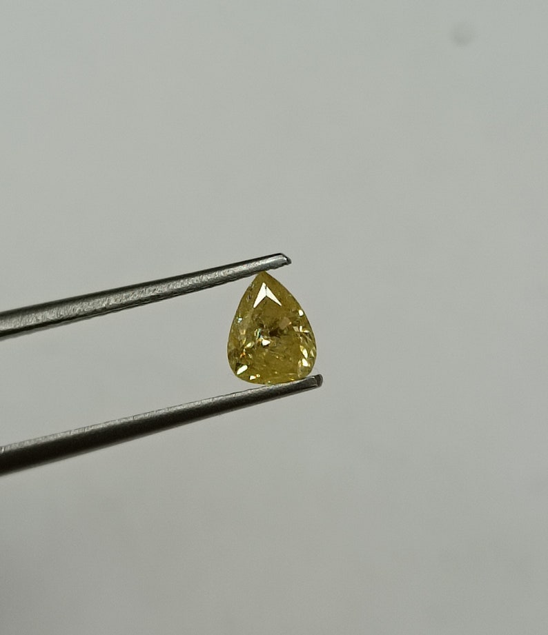May include: A pear-shaped yellow diamond gemstone held by tweezers against a white background.