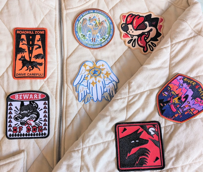 Pu&ograve; includere: Collezione di toppe ricamate con vari disegni, tra cui un lupo, ali d'angelo e un cane dei cartoni animati. Le toppe presentano colori vivaci come rosso, blu e arancione, e alcune includono testo come "ROADKILL ZONE" e "BEWARE".