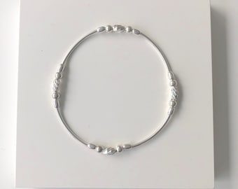 Puede incluir: Un brazalete de plata con pequeñas cuentas redondas. Las cuentas tienen un diseño texturizado.