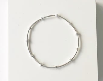 Puede incluir: Un brazalete de plata con pequeñas cuentas redondas espaciadas uniformemente alrededor de la circunferencia.