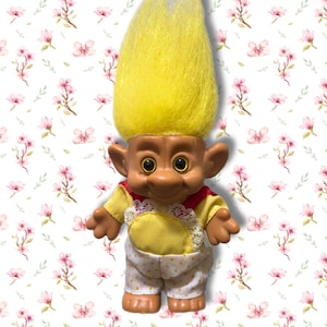 May include: A vintage Troll doll with bright yellow hair. The doll has a tan face, brown eyes, and is wearing a yellow and red outfit with white polka-dot trousers. A classic toy.