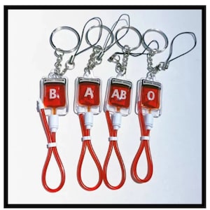 May include: Four red blood bag keyrings with different blood types: B, A, AB, and O. Each keyring has a silver ring and a red string.