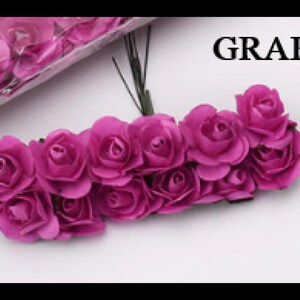 Puede incluir: Un grupo de 15 peque&ntilde;as rosas de papel artificiales de color morado oscuro. Las rosas est&aacute;n unidas a tallos finos de alambre y est&aacute;n dispuestas en semic&iacute;rculo. El texto "GRAPE" es visible en el fondo.