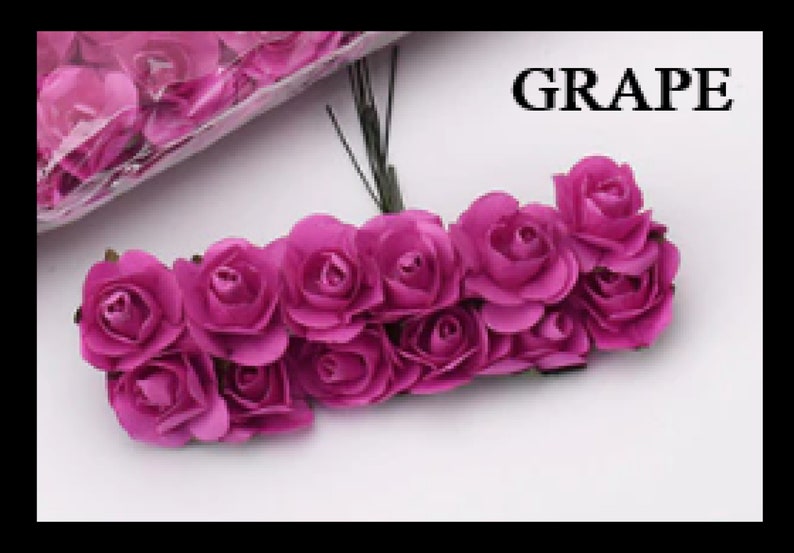 Puede incluir: Un grupo de 15 peque&ntilde;as rosas de papel artificiales de color morado oscuro. Las rosas est&aacute;n unidas a tallos finos de alambre y est&aacute;n dispuestas en semic&iacute;rculo. El texto "GRAPE" es visible en el fondo.